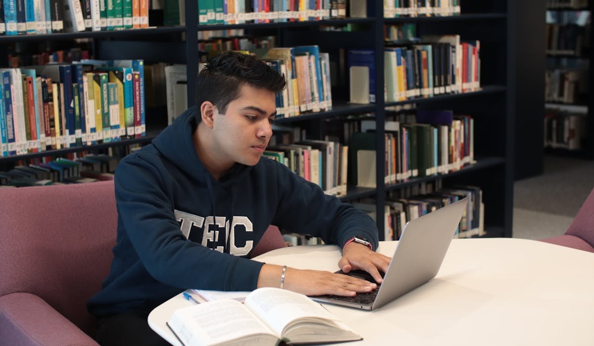 Student working on laptop in library - Mac vs PC for students comparison